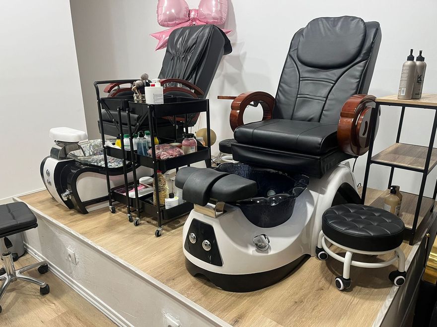 Estación de pedicura tipo spa con dos sillones de masaje negros, bañeras para pies y herramientas para uñas en una cabina de salón.