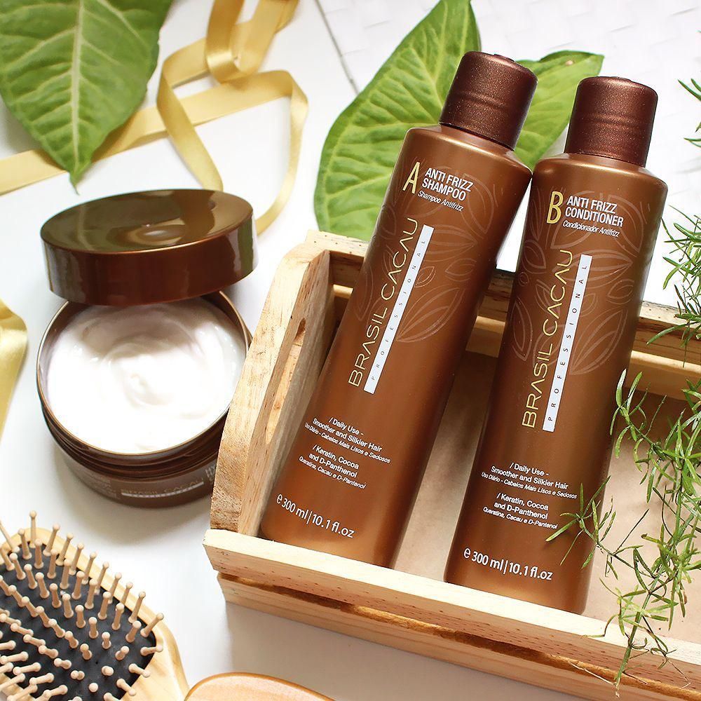 Frascos marrones para el cuidado del cabello en una bandeja de madera junto a un tarro de crema, un peine y hojas sobre un fondo claro.