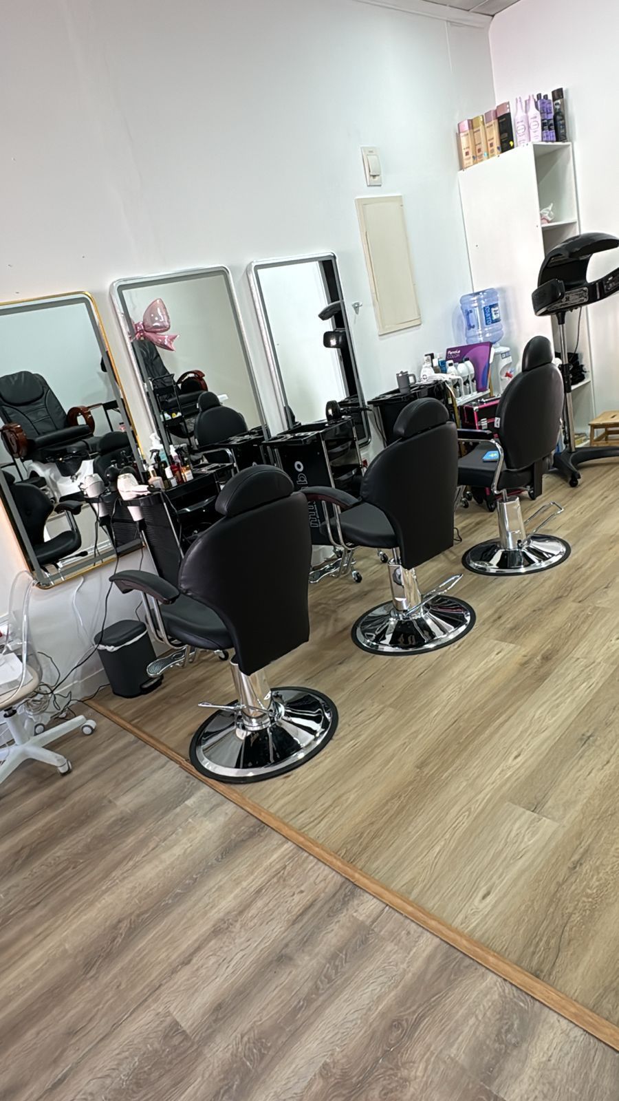 Interior de salón moderno con sillones de peluquería negros, espejos y estaciones de peluquería sobre suelo de madera.