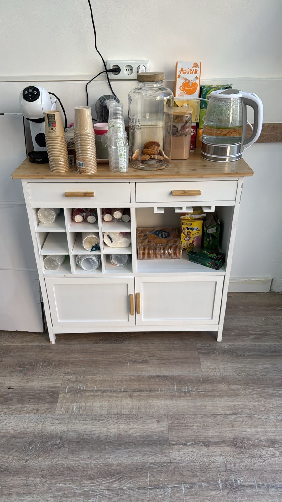 Mueble de cocina blanco con cafetera, tazas, jarros, hervidor y tarros en la parte superior; almacenamiento organizado en la parte inferior.