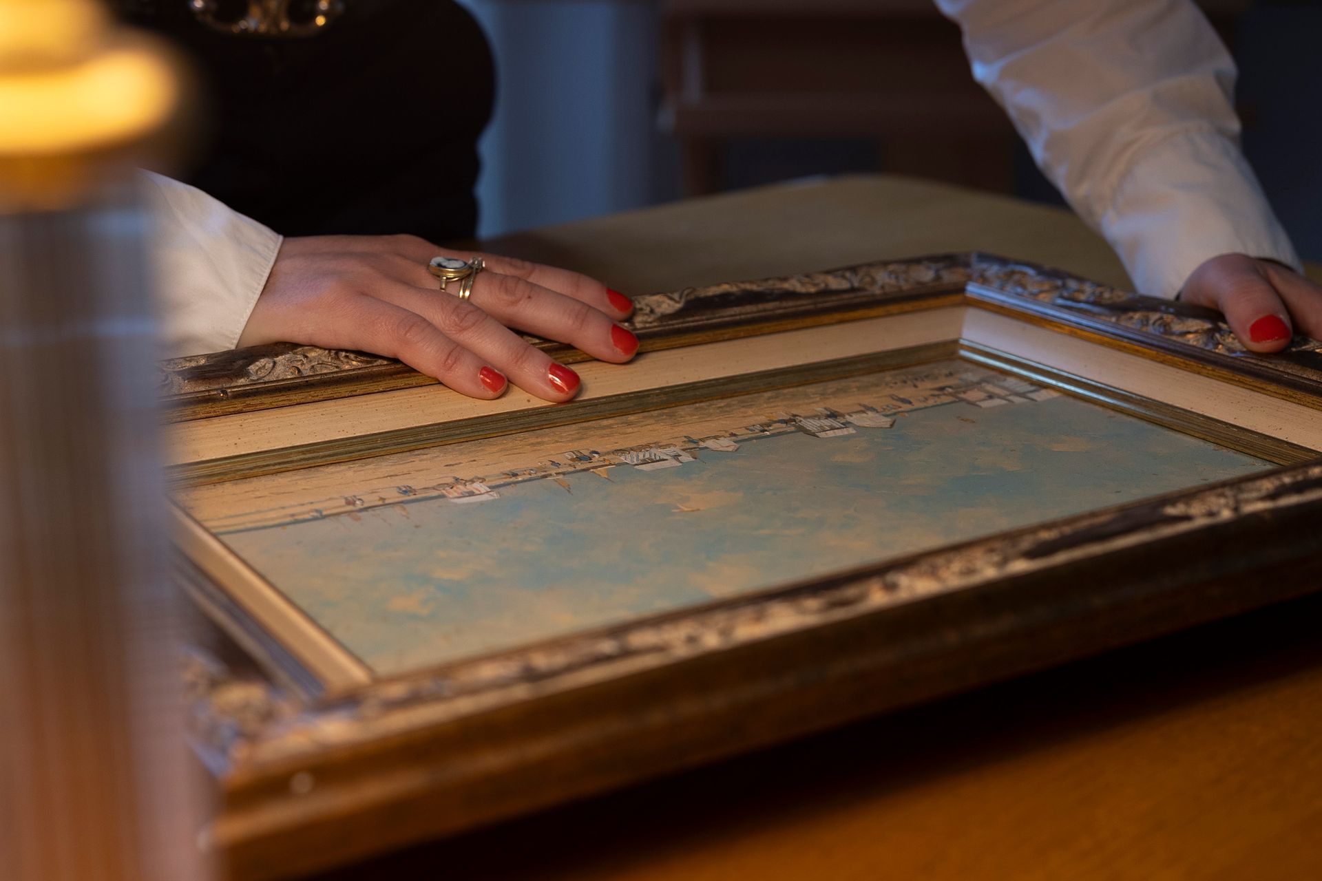 Une personne pose sa main sur la bordure du cadre d'un tableau posé sur un bureau.