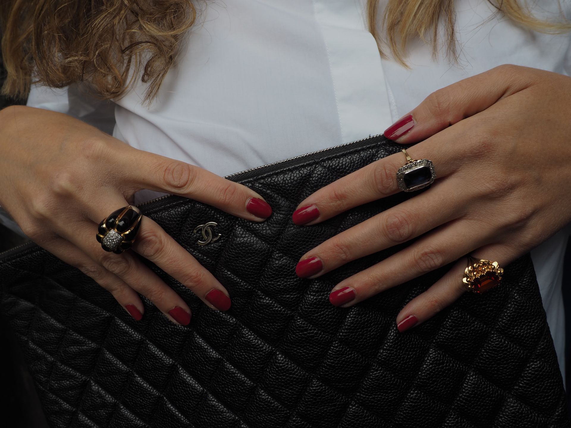 Mains de femme aux ongles rouges et aux bagues tenant un sac à main matelassé noir.