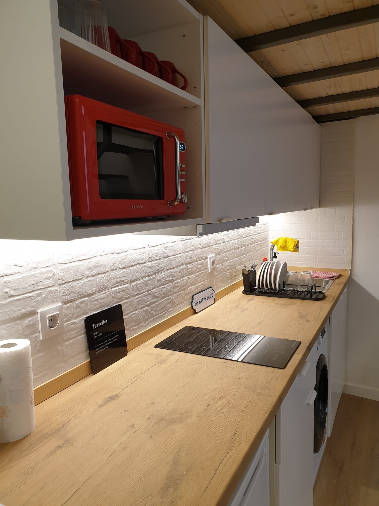 Una cocina pequeña con encimera de madera, salpicadero de ladrillo blanco y un microondas rojo. 