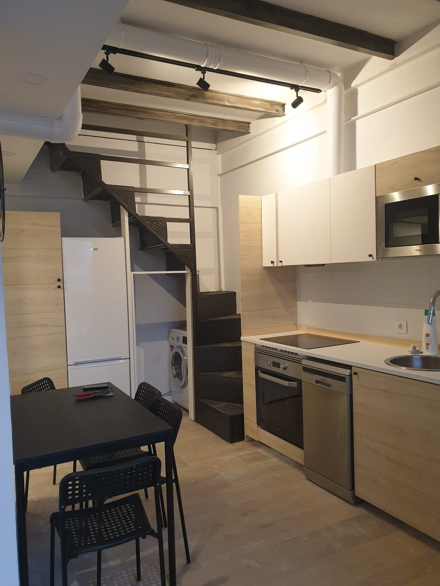 Un pequeño apartamento con cocina, comedor y escalera a un loft. 