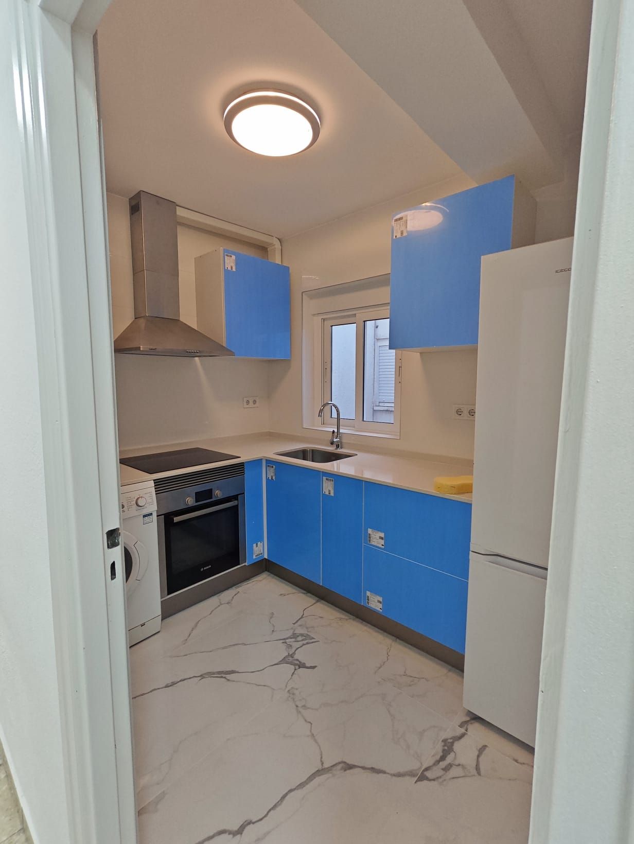 Una cocina pequeña y moderna con gabinetes azules, encimeras blancas y electrodomésticos.