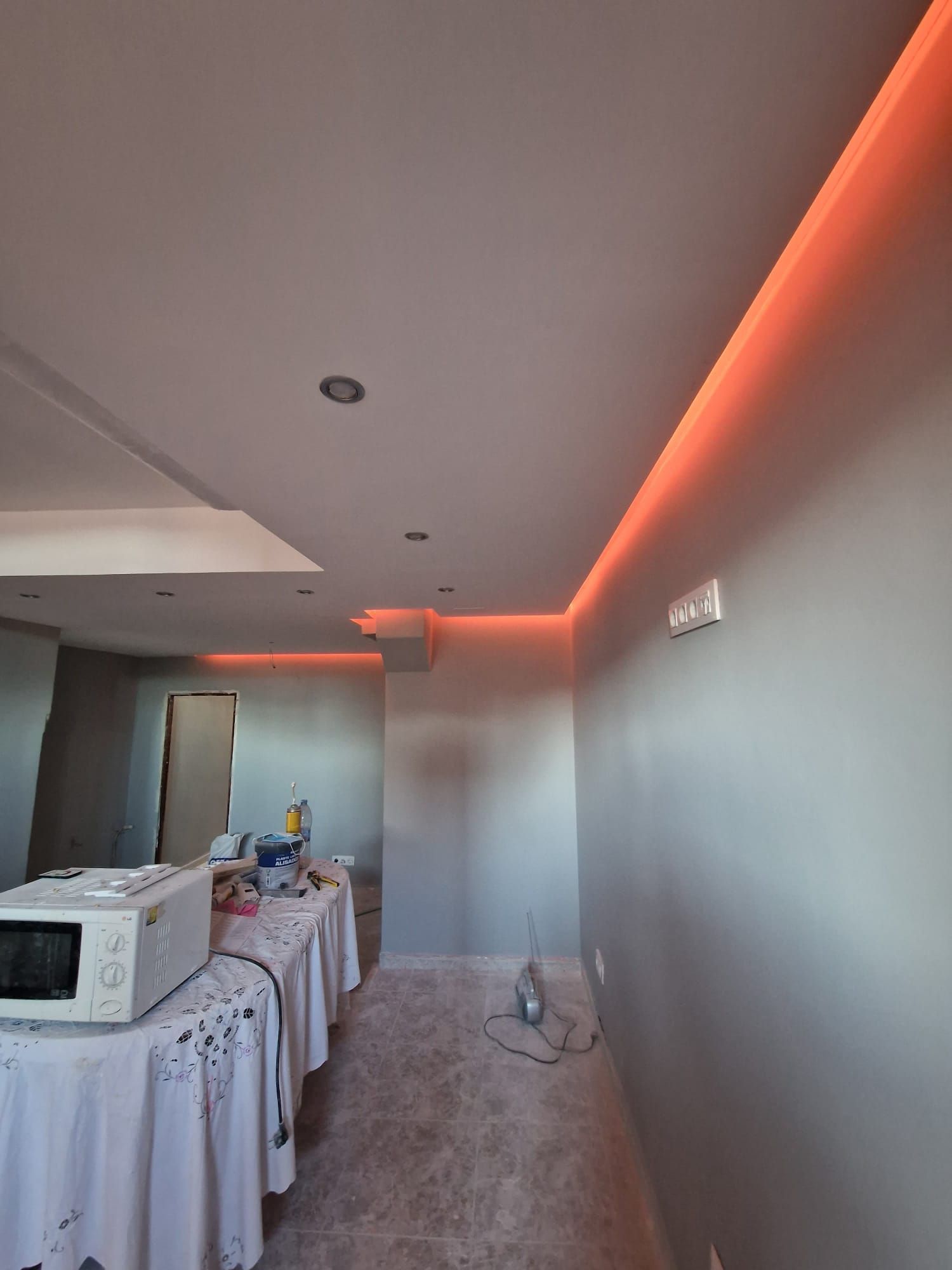 Una habitación con techo blanco, iluminación ambiental roja y paredes grises. Un microondas y una mesa están en primer plano.