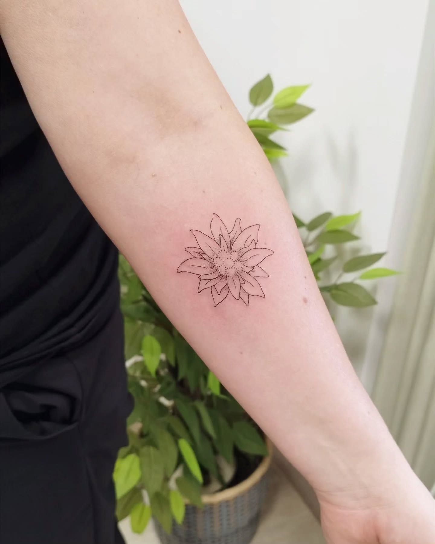 Una mujer tiene un pequeño tatuaje de flor en su antebrazo.