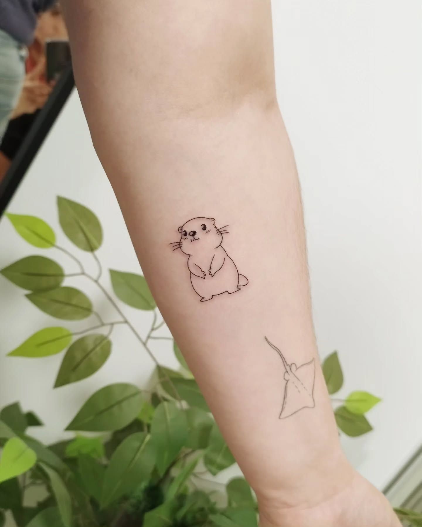 Un pequeño tatuaje de un hámster y una raya en el brazo de una persona.