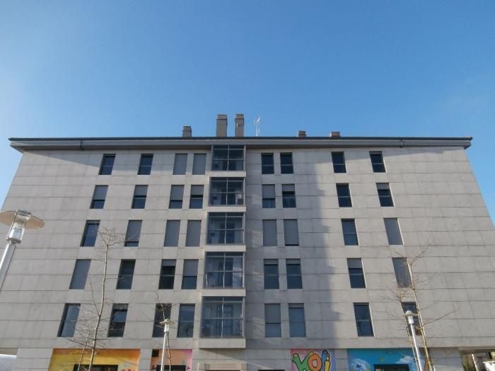 Edificio de apartamentos gris con múltiples ventanas contra un cielo azul claro.