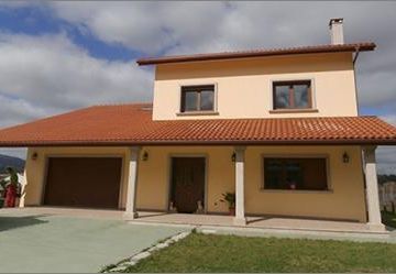 Casa de dos pisos con techo de tejas de barro, puerta de garaje y césped bajo un cielo parcialmente nublado.