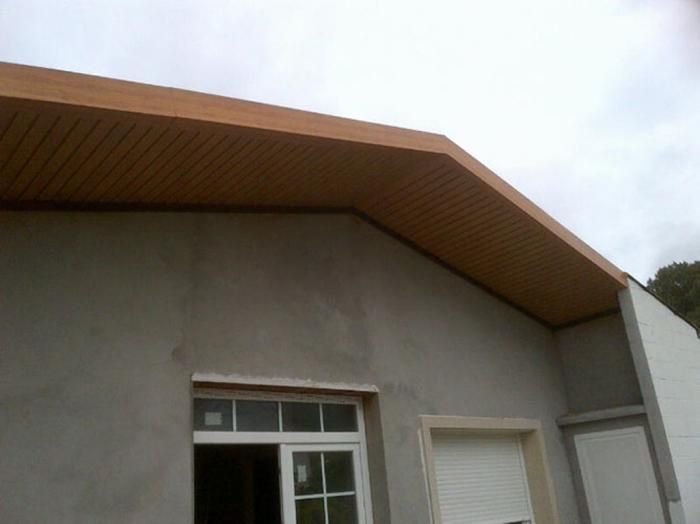 Exterior del edificio con plafón marrón claro y paredes de estuco gris, cielo nublado.