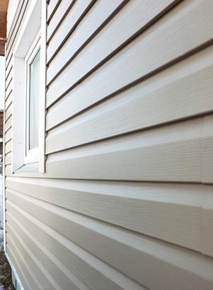 Revestimiento beige en una casa con marco de ventana blanco; perspectiva de primer plano.