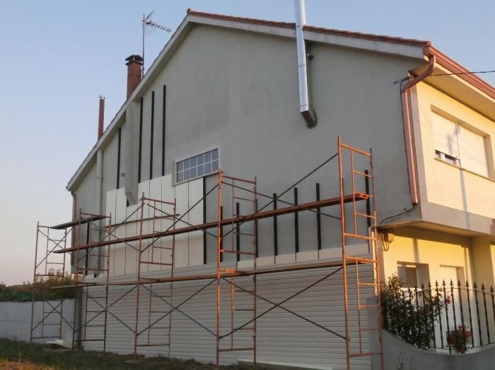 Casa con andamios, en proceso de renovación exterior. Revestimiento beige, chimenea y canalones metálicos visibles.