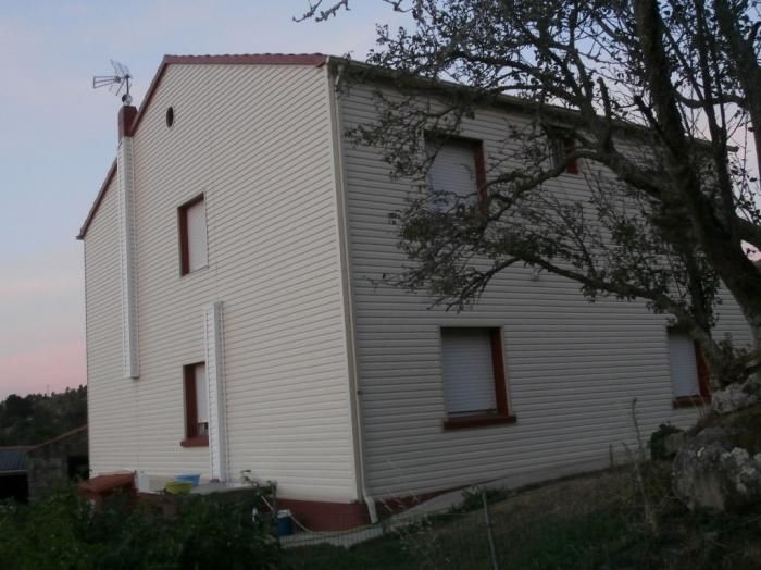 Casa de dos plantas con revestimiento blanco roto, ventanas con molduras rojas y chimenea. Antena en el tejado.