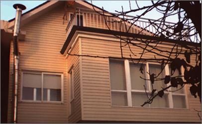 Casa color canela con balcón, ventanas con marcos blancos y ramas de árboles en primer plano.