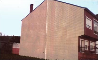 Edificio de ladrillo beige al lado de un edificio granate, con chimenea y ventanas.