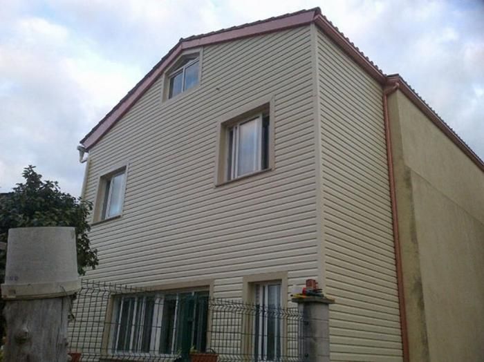 Un revestimiento beige cubre una casa de dos pisos con molduras de techo rojas.