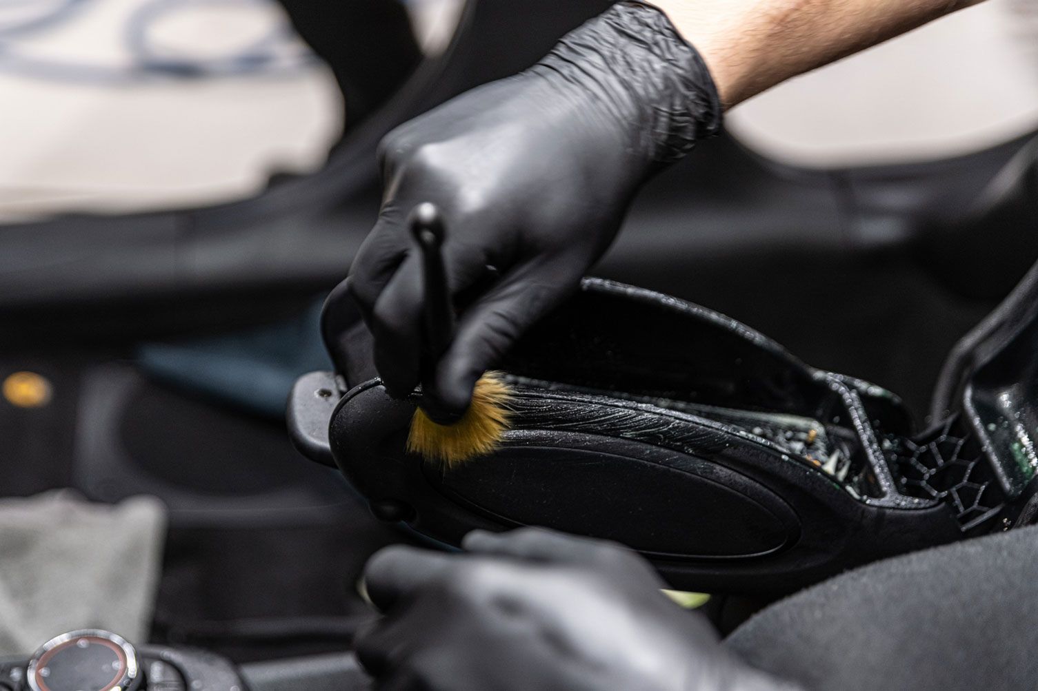 Manos enguantadas limpiando el interior de un coche con un cepillo.