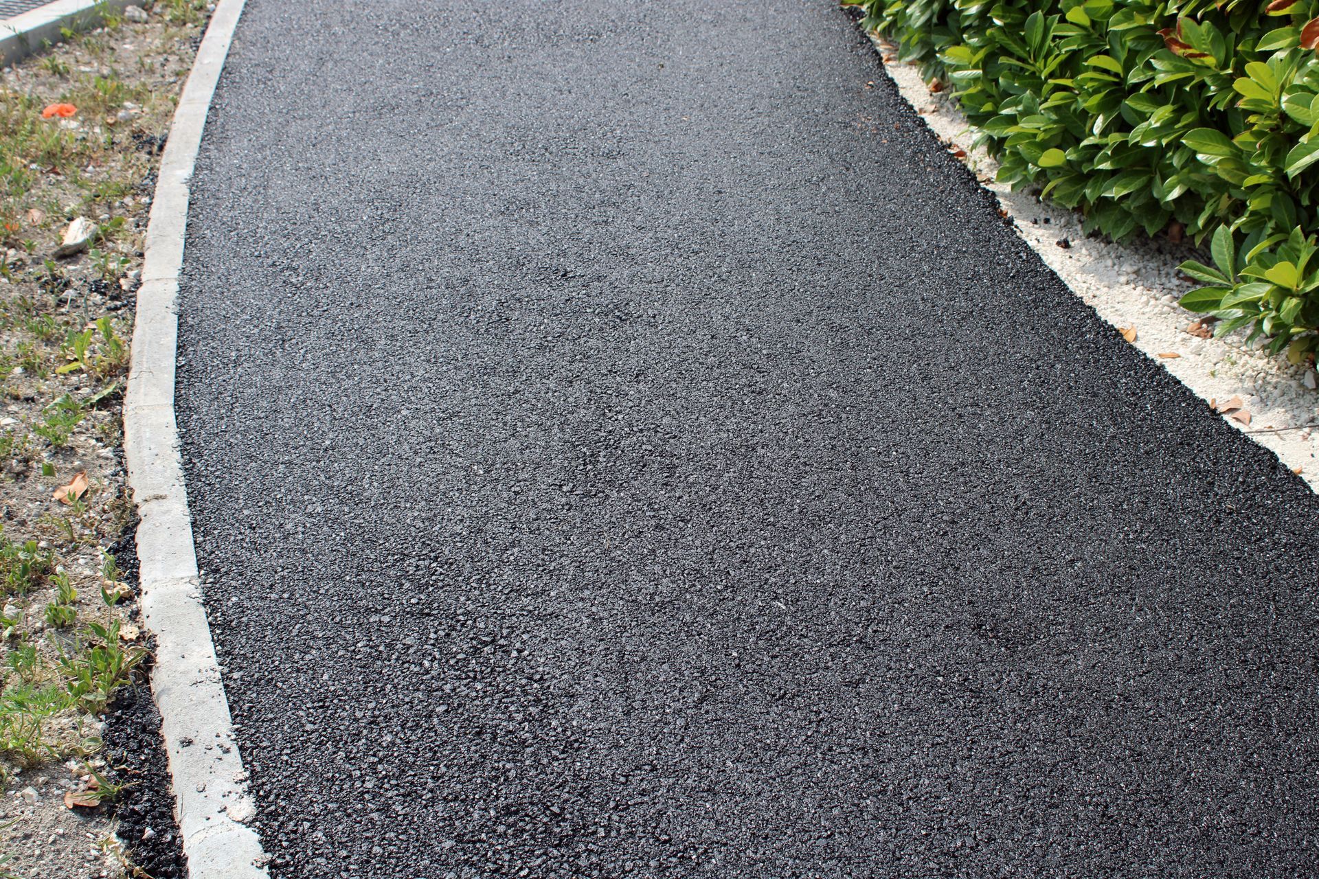 Allée pavée de noir avec bordure en béton, bordée de pelouse.
