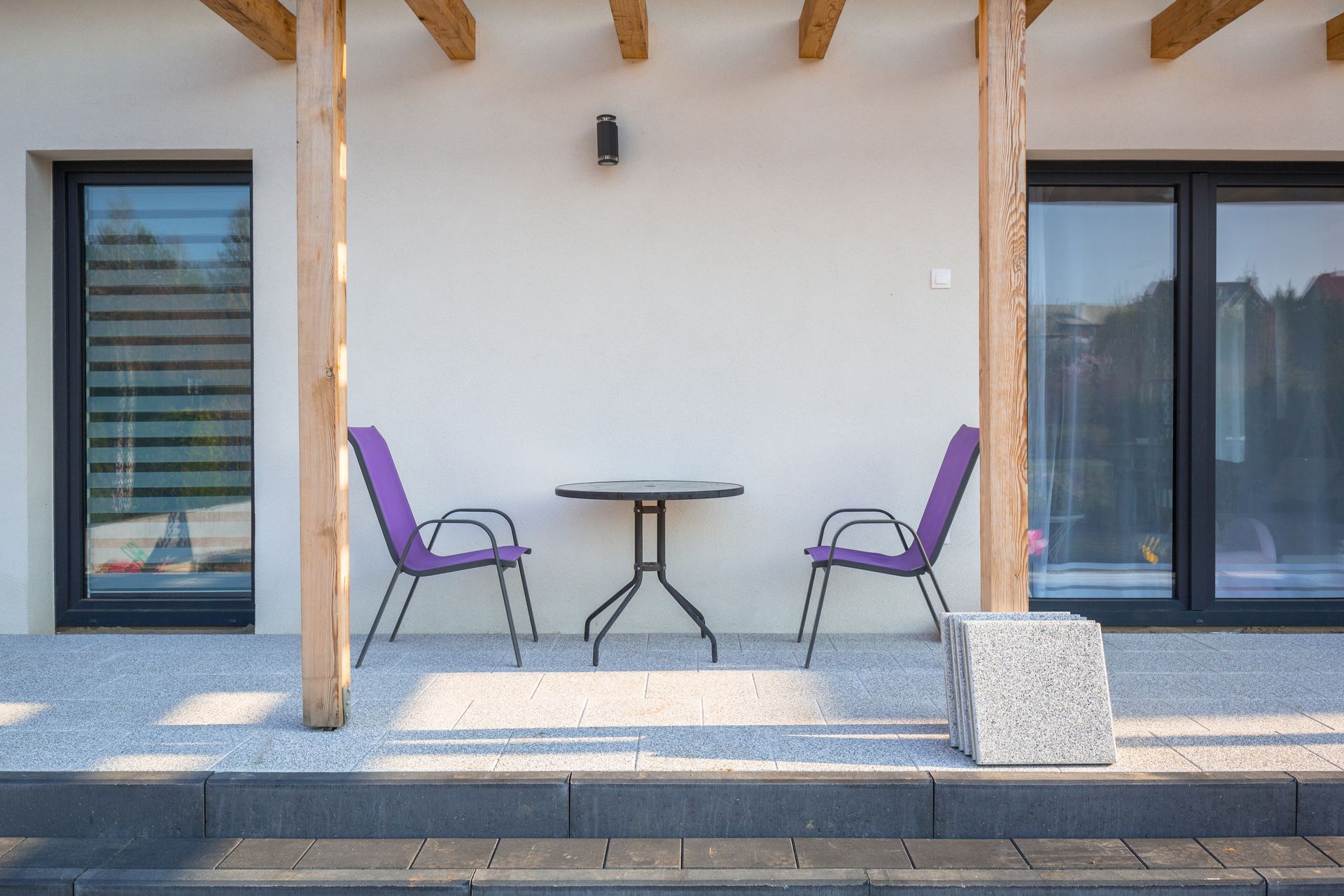 Un patio avec deux chaises violettes et une petite table sous une pergola en bois.