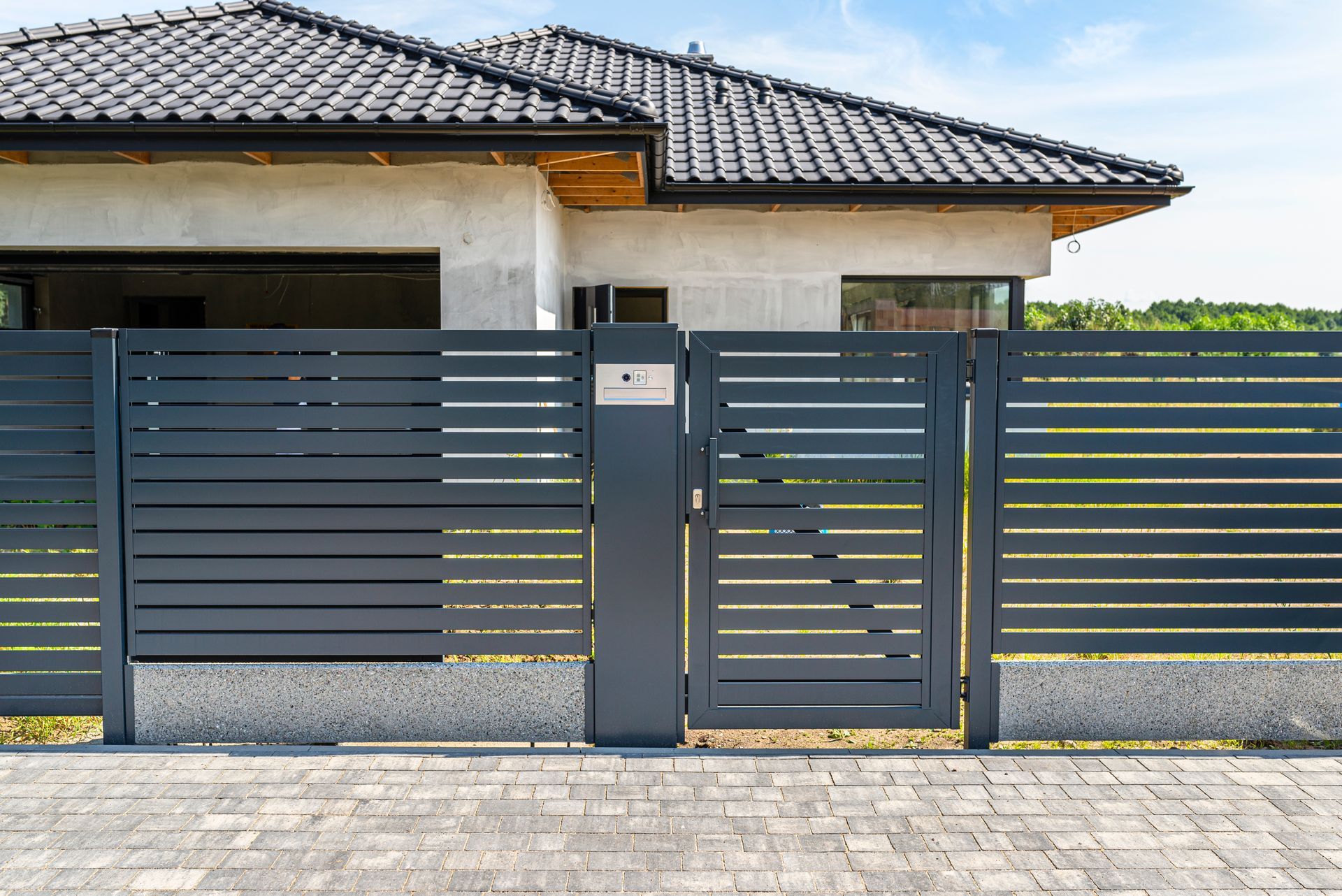 Clôture à lattes horizontales grises avec portail devant une maison moderne, allée pavée.