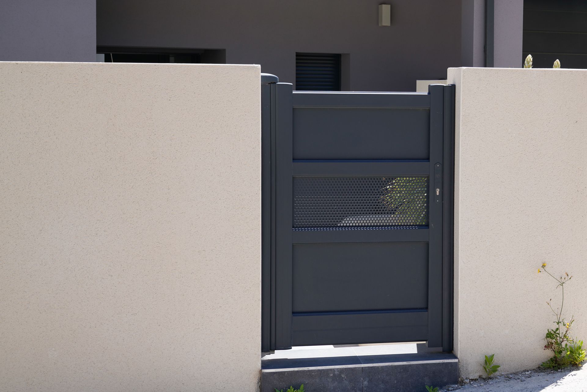 Portail gris encastré dans des murs en stuc beige.