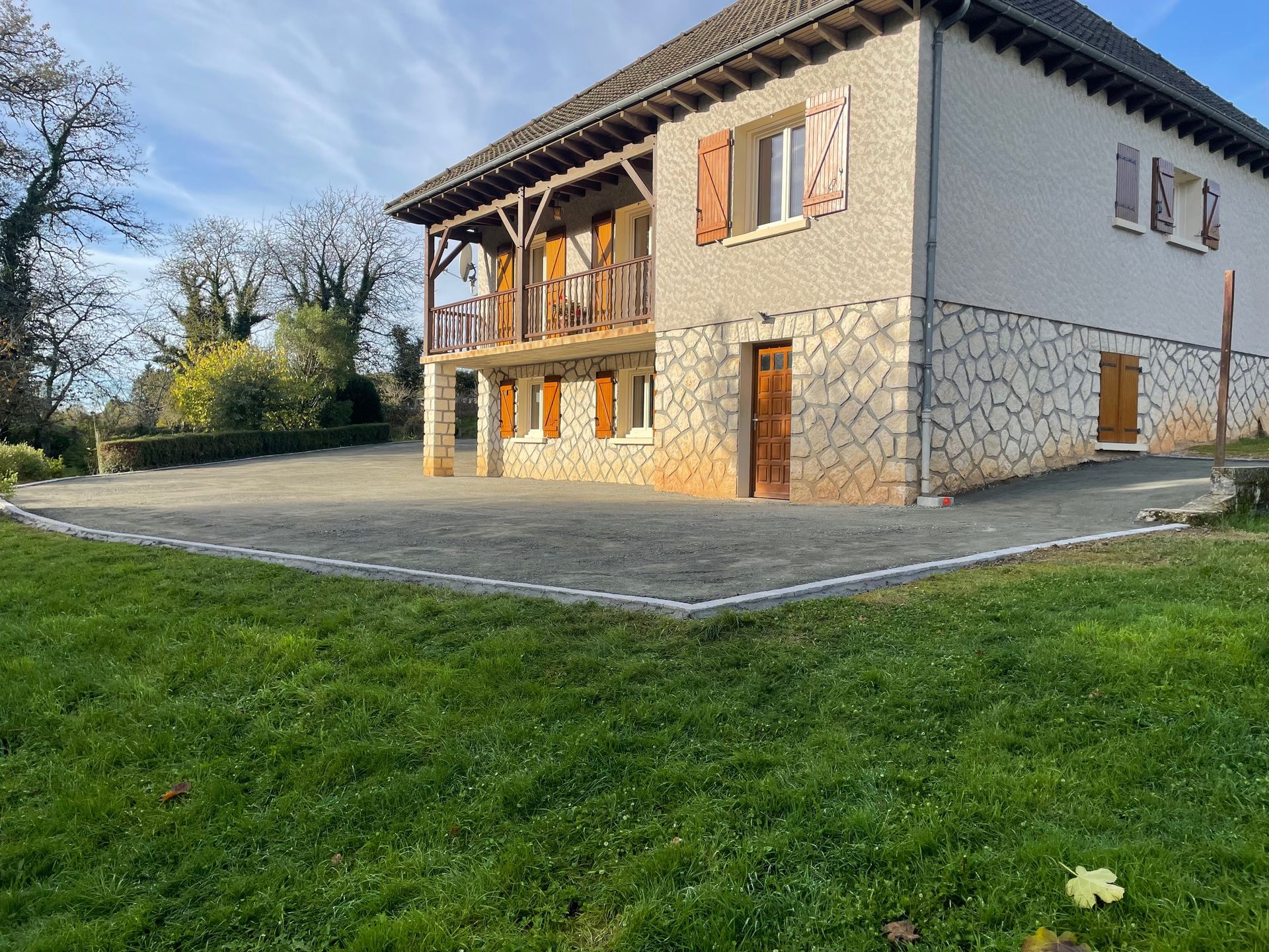 Allée de gravier bordée de galets argentés, jouxtant un bâtiment beige avec une porte de garage grise fermée.