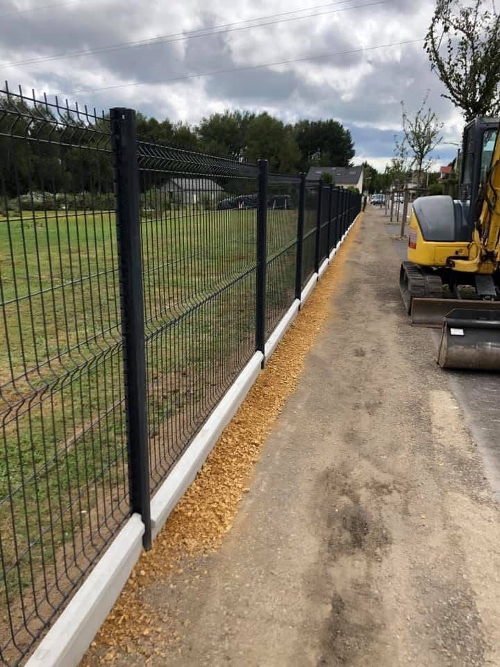 Clôture en fil de fer vert devant des arbustes verts, le long d'une allée pavée et de pelouse.