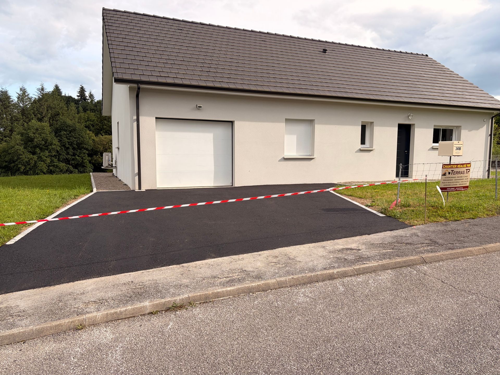 Allée pavée de noir avec bordure en béton, bordée de pelouse.