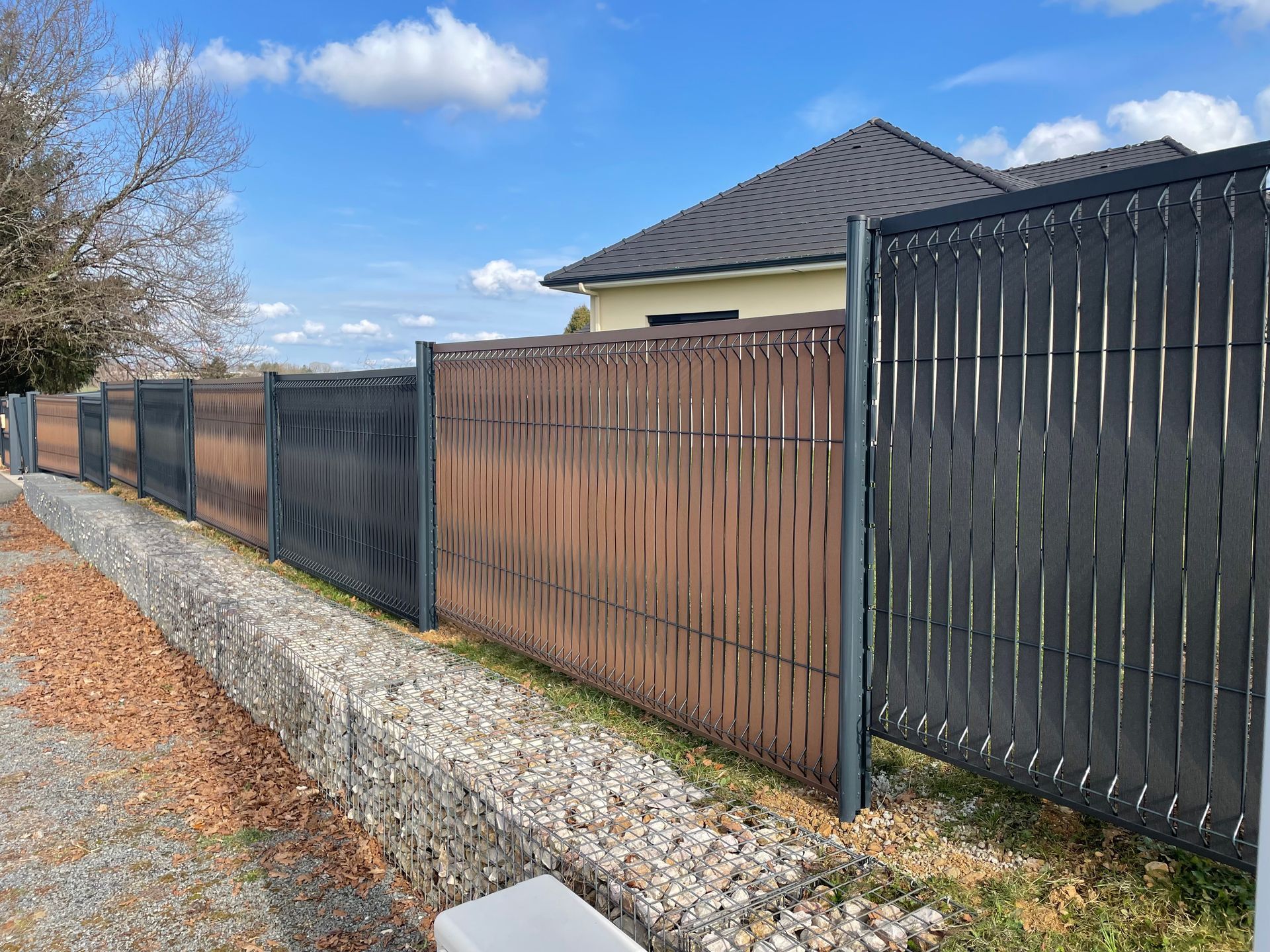 Une clôture moderne composée de lattes verticales gris foncé et marron le long d'une limite de propriété.