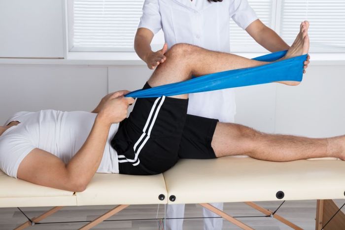 Der Therapeut begleitet einen Patienten, der Übungen mit einem Dehnungsband für sein Knie durchführt.