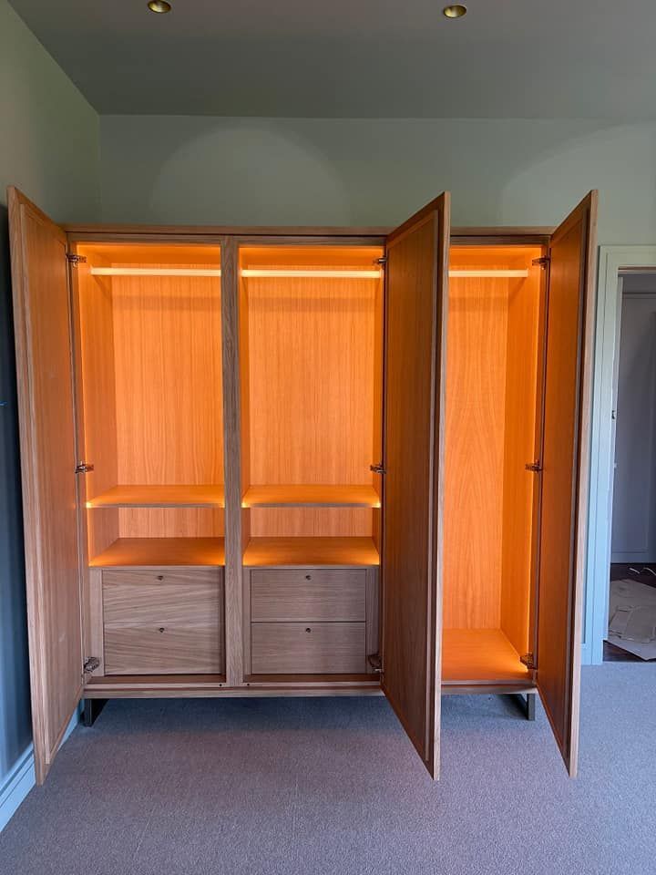 Armario de madera con tres puertas abiertas, interior iluminado con luz cálida, dos cajones vistos.