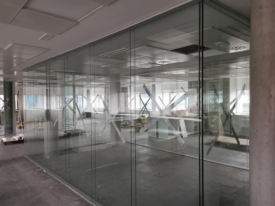 Espacio de oficina en construcción con paredes de cristal, soportes visibles y elementos sin terminar.