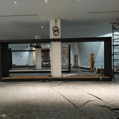 Obra interior con estructura de marco negro, andamios y piso de concreto.