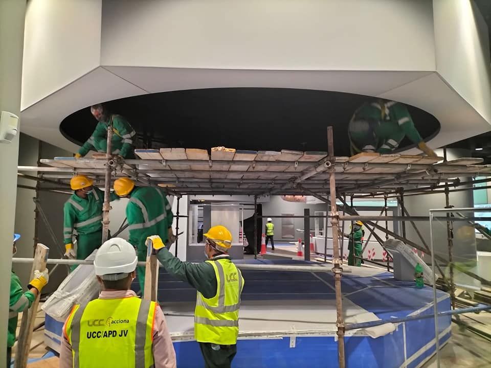 Obreros de la construcción con equipo de seguridad verde y amarillo en un andamio, trabajando en un techo circular.