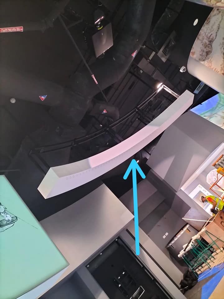 Una viga curva blanca está suspendida de un techo oscuro, con una flecha apuntando hacia ella.