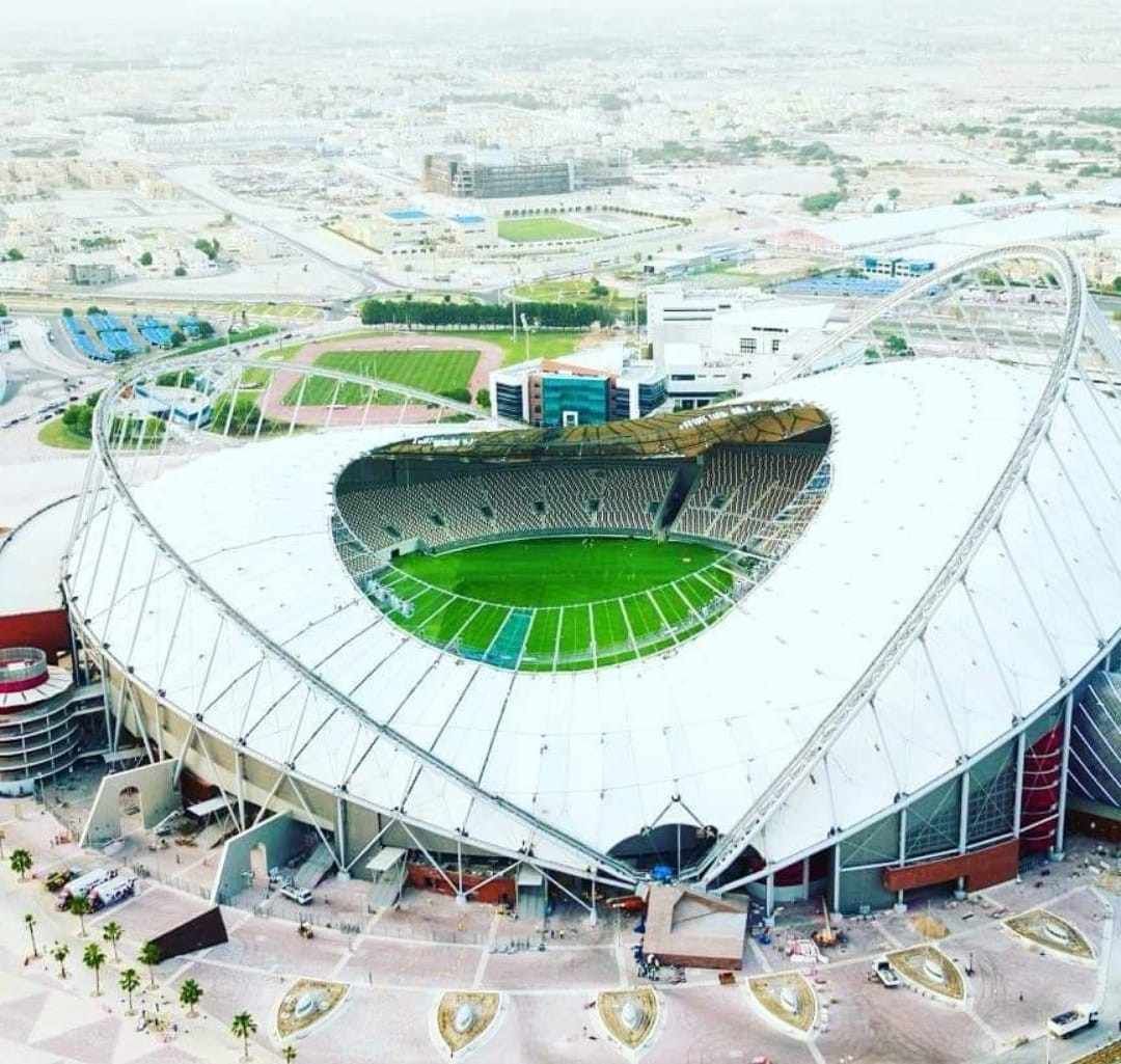 Vista aérea de un estadio con campo verde, techo blanco y paisaje urbano circundante.