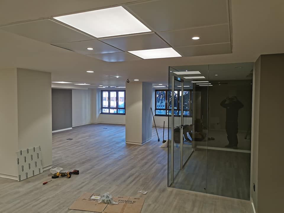 Espacio de oficina vacío con una habitación con paredes de vidrio, luces de techo brillantes y pisos de madera.