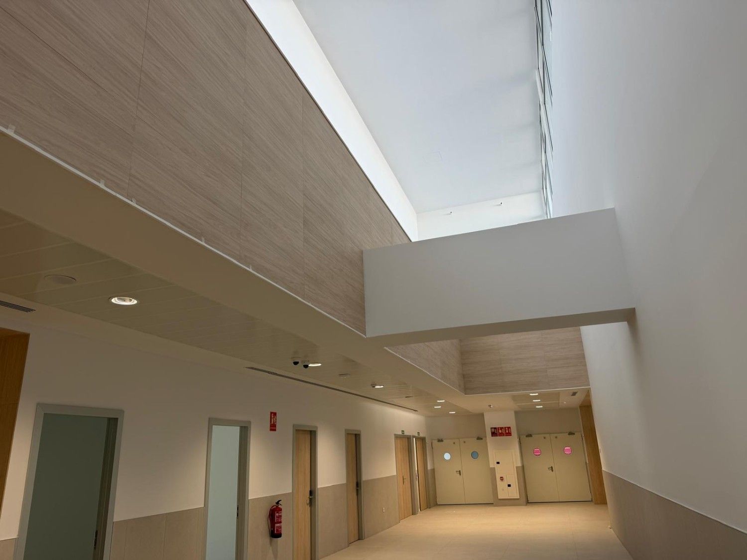 Pasillo interior con techos altos, puertas y panel decorativo de madera.