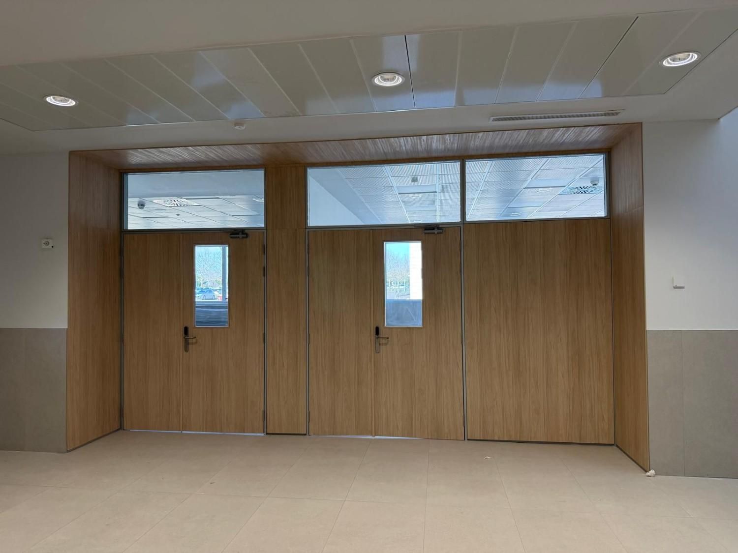 Dos puertas de madera con paneles de vidrio y un travesaño encima, colocadas en una pared de color claro.