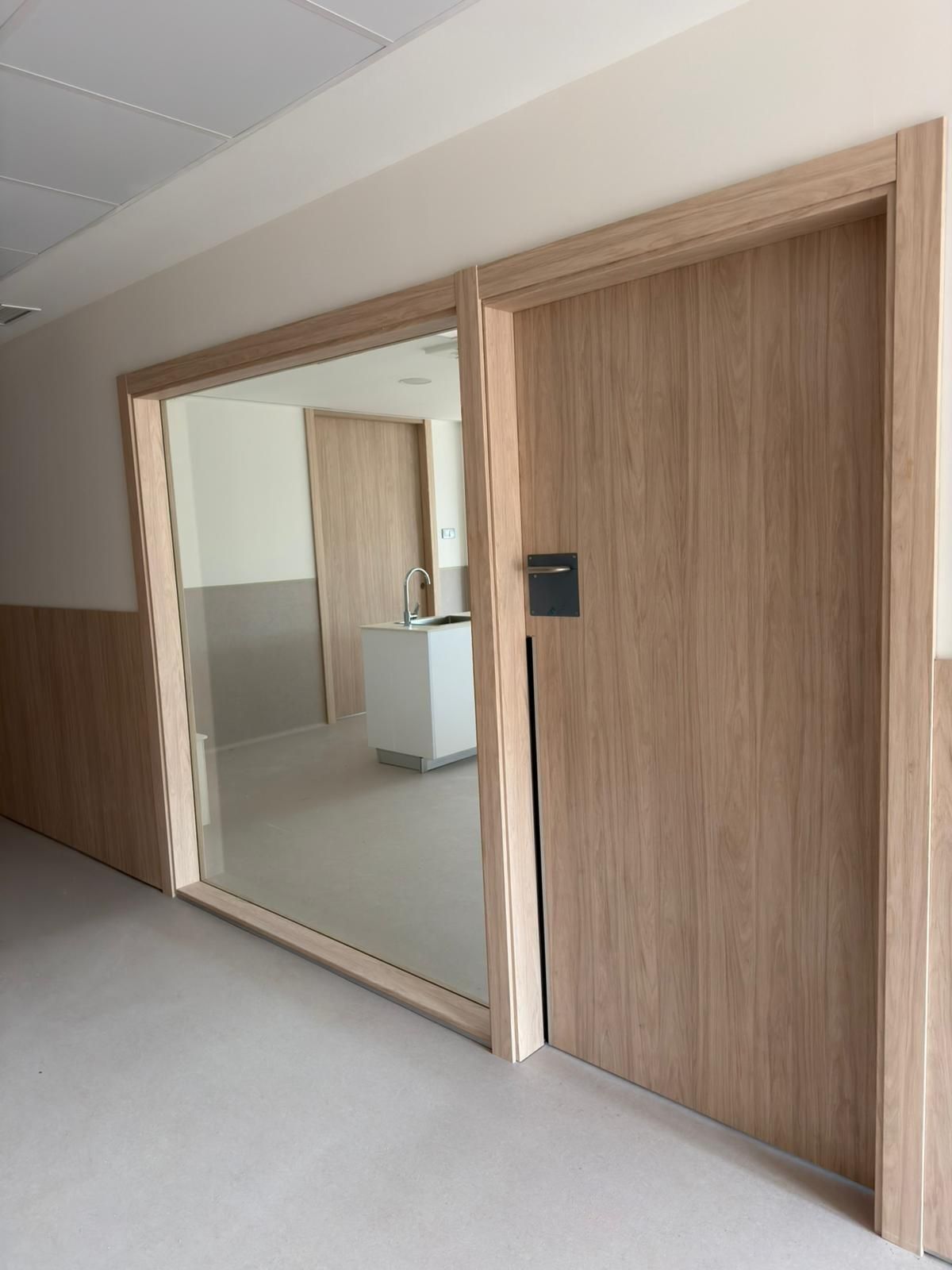 Pasillo con dos puertas de madera. Una es maciza y la otra tiene una gran ventana que da a la cocina.