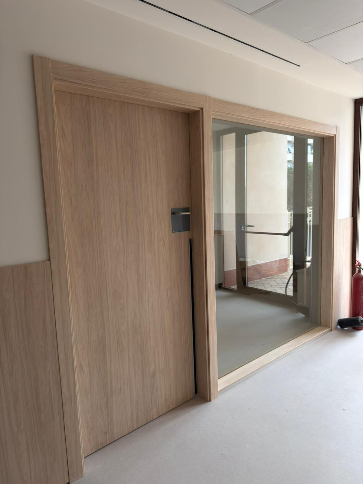 Puerta de madera y puerta de cristal en un pasillo. Paredes blancas y beige.