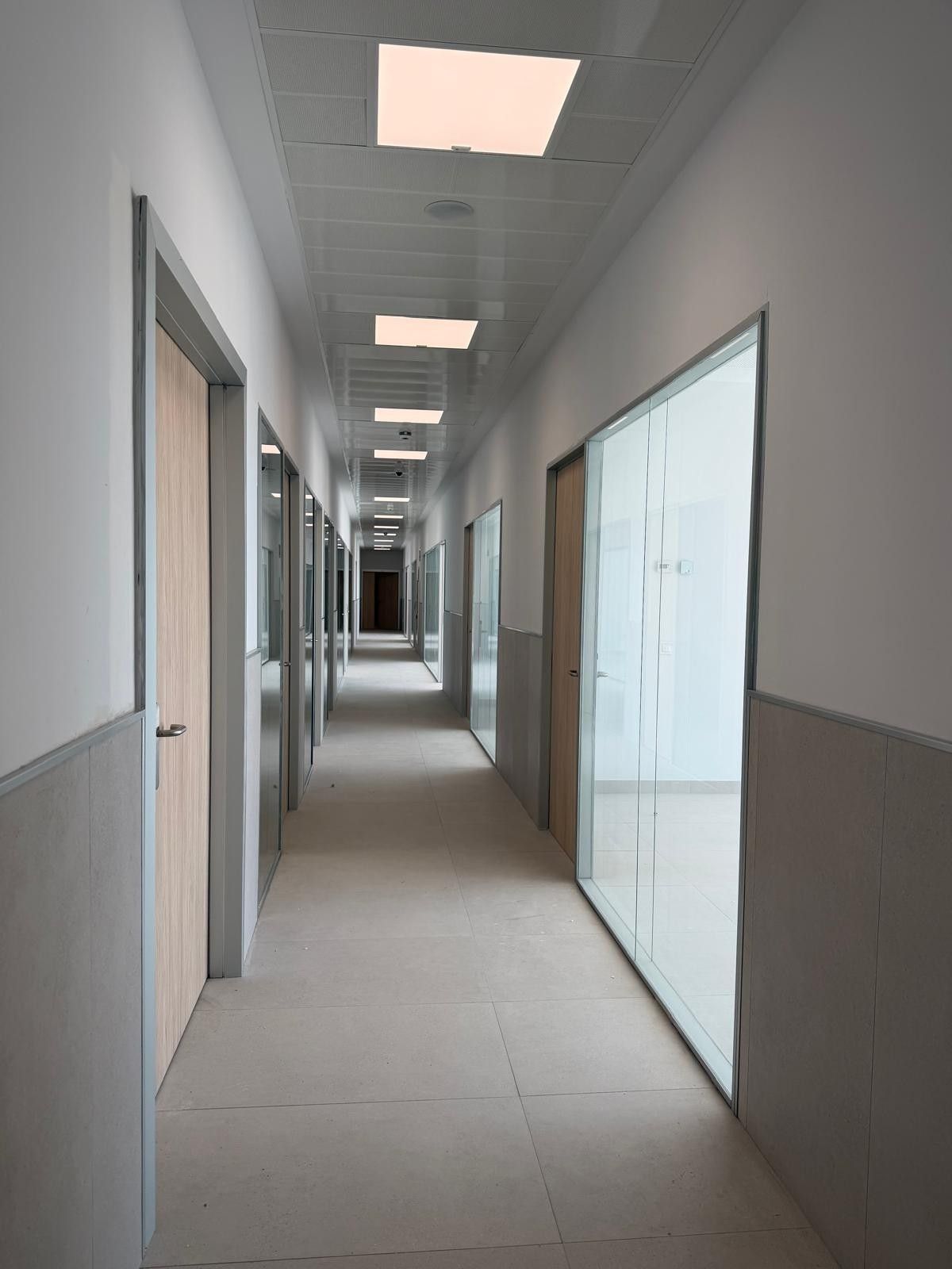 Interior de una habitación en construcción con paredes grises, piso de madera clara y luces de techo rectangulares.