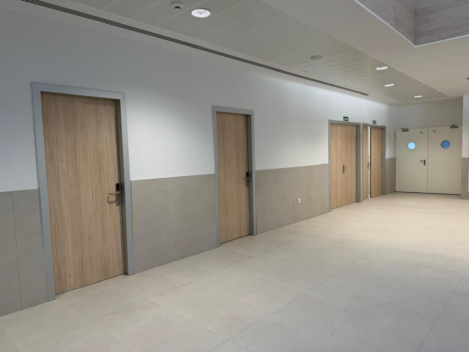 Pasillo con múltiples puertas de madera clara y pared blanca y gris.