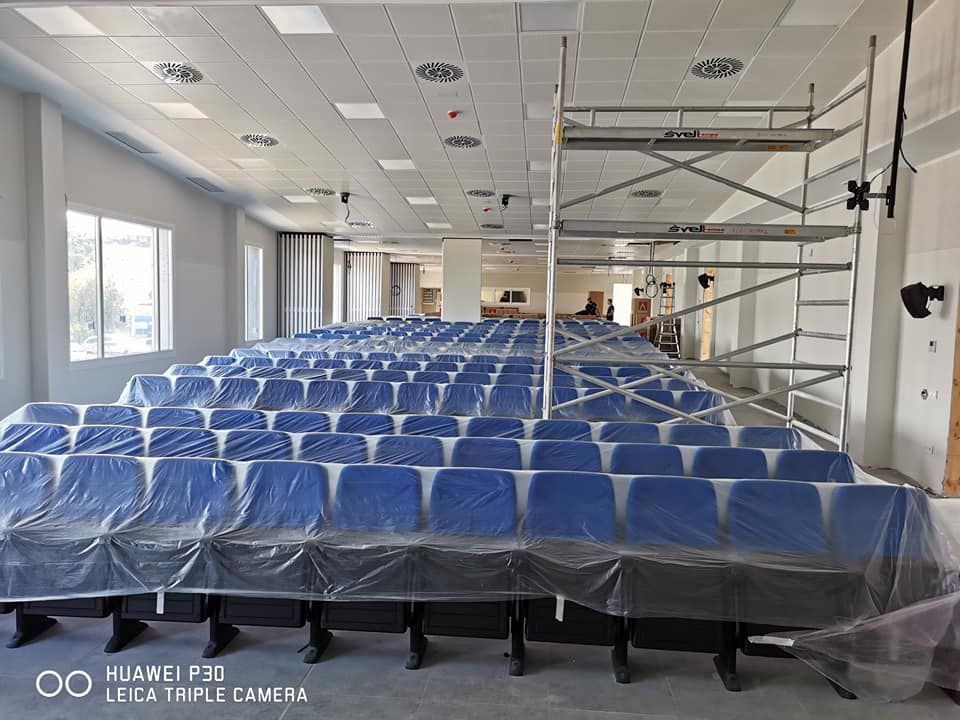 Auditorio con filas de asientos azules cubiertos de plástico, andamios y luces de techo.