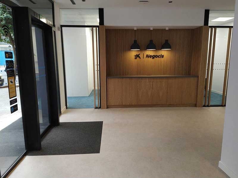 Entrada a un negocio, con revestimiento de madera, mostrador de recepción y puertas de cristal.