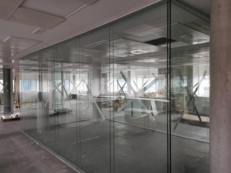 Vista interior de un espacio de oficina moderno con paredes de vidrio, algunas grabadas con patrones geométricos.