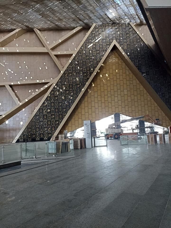 Interior de un edificio con diseño geométrico de madera y azulejos, paneles de vidrio y materiales de construcción.