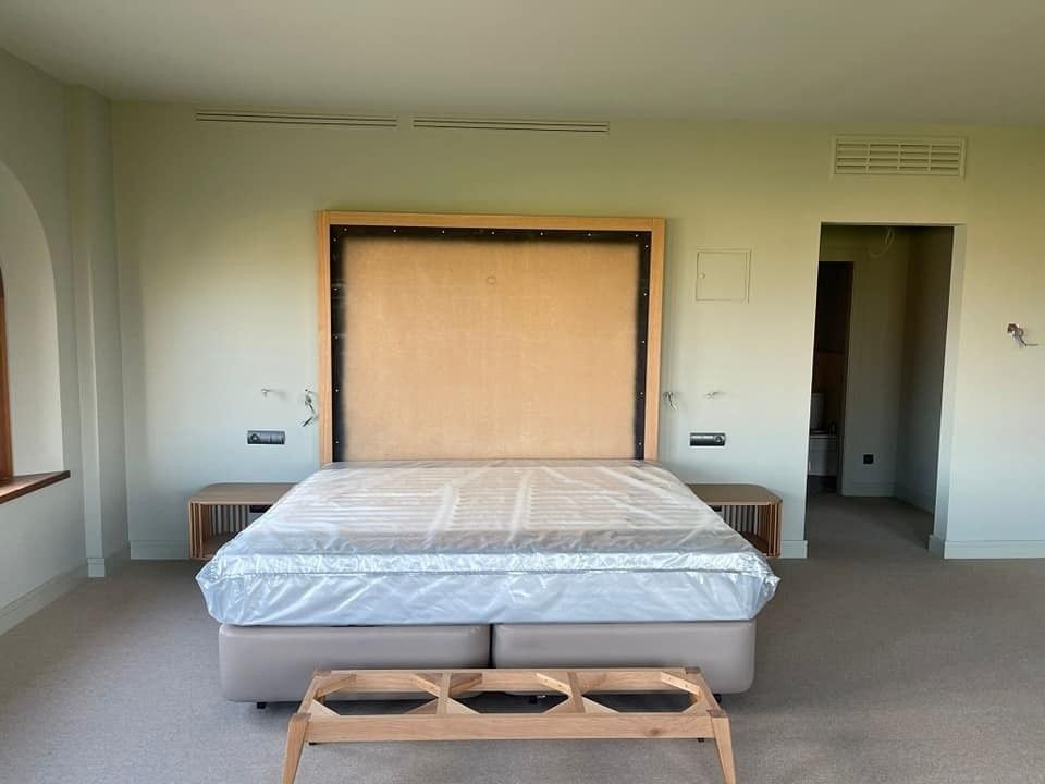 Dormitorio con cama revestida en plástico, mesitas de noche, cabecero y puerta.