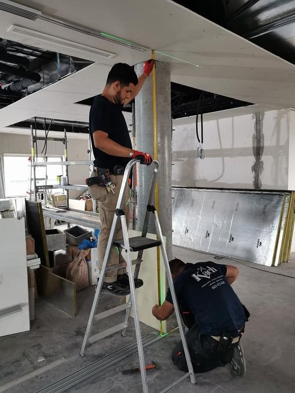 Dos trabajadores de la construcción miden y trabajan en una columna y un techo en un edificio sin terminar.